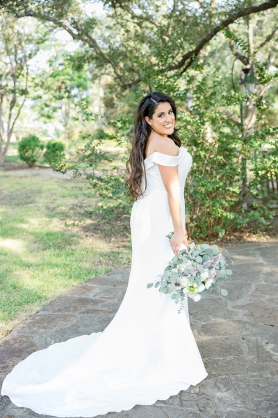 San Antonio bride looks over her shoulder at the camera while holding her bouquet pointed at the ground. Her San Antonio wedding makeup looks incredible