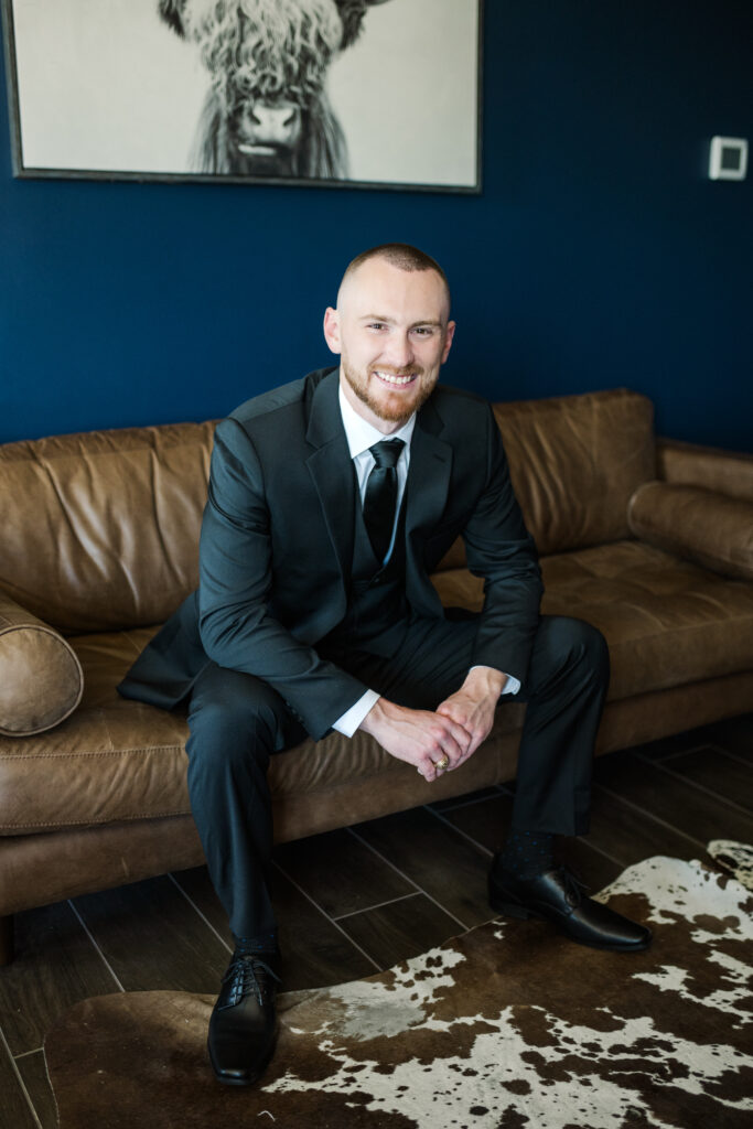 Groom sits in the getting ready room on a couch at the Gardenia Venue