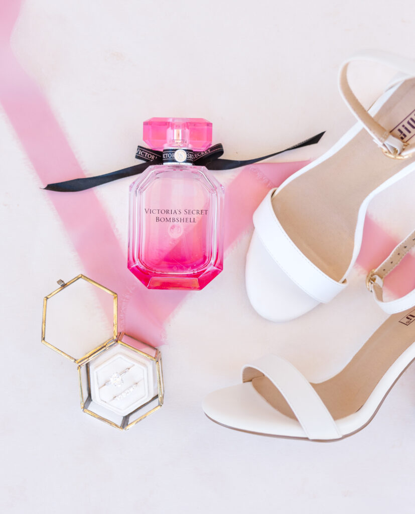 San Antonio wedding flat lay consisting of a ring box with an engagement ring and band, white high heeled, open toed shoes, and a Victoria Secret perfume 