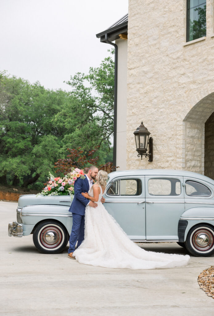 Bride and groom kiss in front of a blue vintage car outside of The Preserve at Canyon Lake which is one of the best San Antonio wedding venues