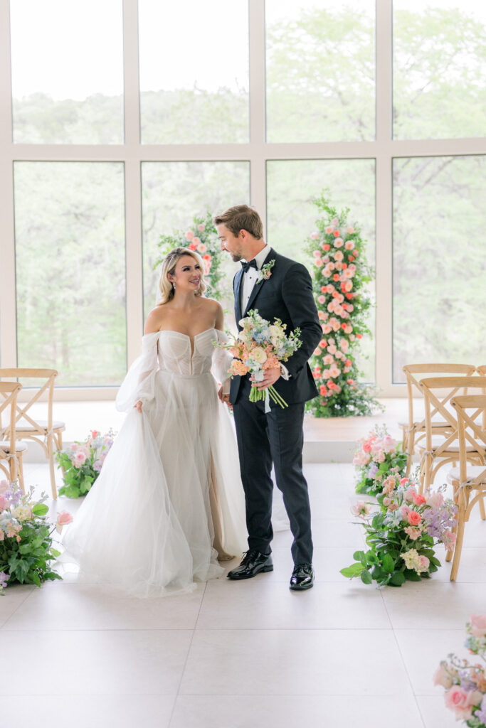 Bride and groom look into each others eyes holding hands in front of a wall of large glass windows at The Preserve at Canyon Lake - a San Antonio wedding venue