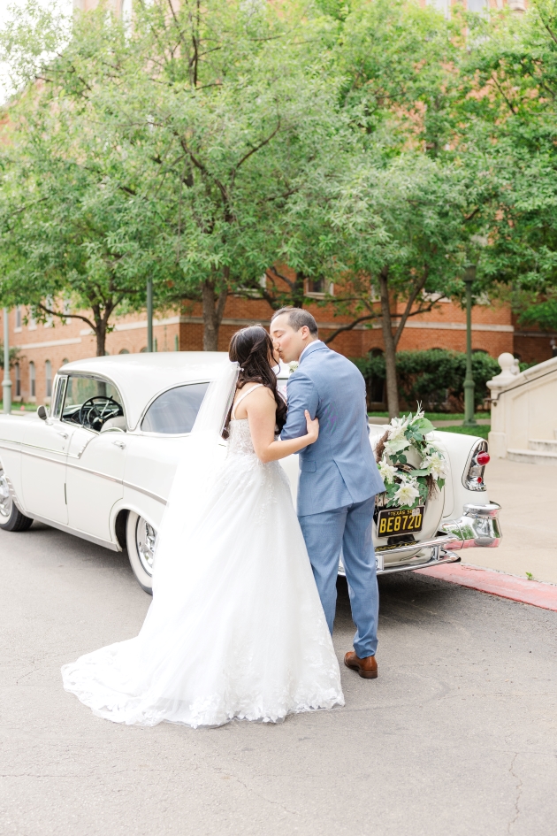 Bride pulls groom in for a beautiful kiss in front of their getaway car in front of their San Antonio wedding venue