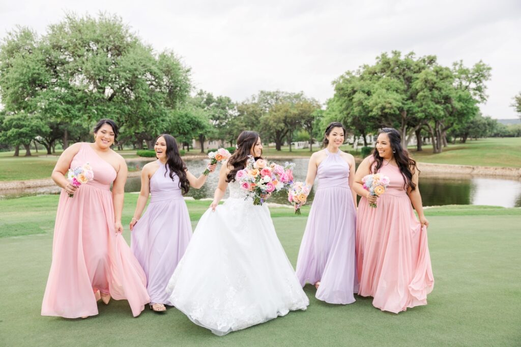 Bride walks away from pond with bridesmaids in lavender and light pink dresses at a San Antonio wedding venue