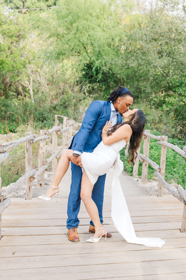 Man dips his fiancé in a grove of trees on a wooden bridge in this San Antonio engagement photo 