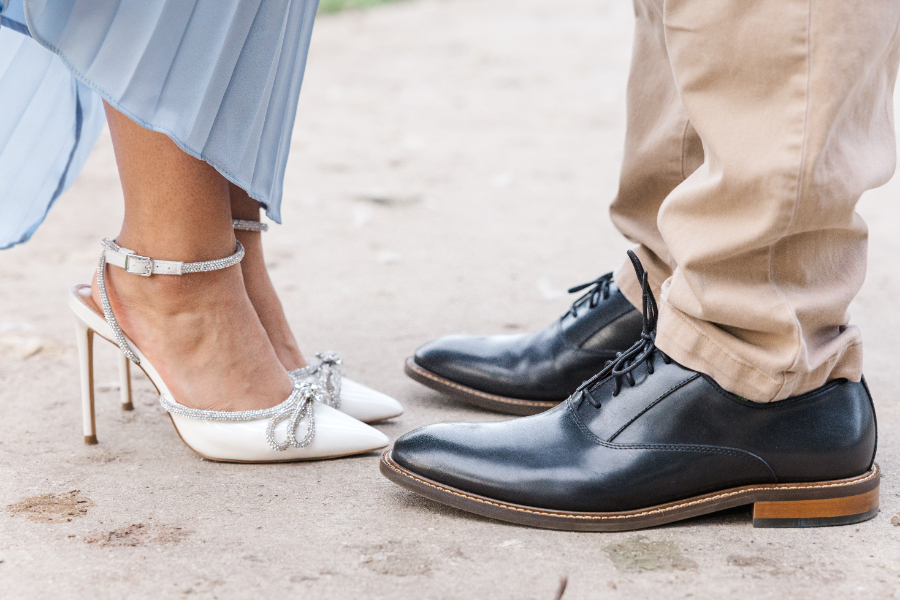 In this San Antonio engagement photo, the bride to be shoes off her bejeweled white heels as she stands next to her fiancé wearing black loafers. The photo cuts off at their mid calves