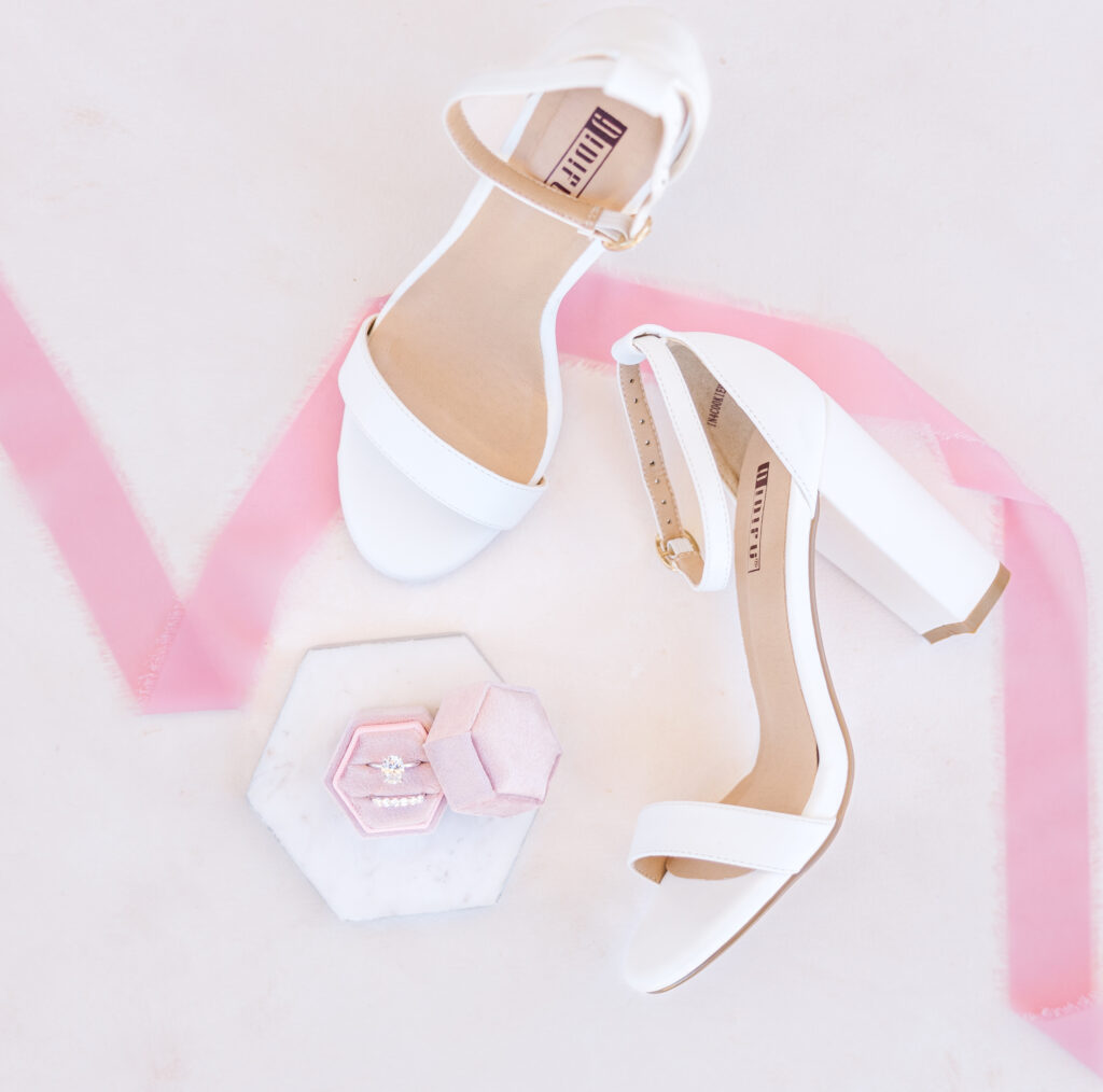 Engagement ring and wedding band, shoes, and a ribbon carefully laid on a mat for some detail wedding flat lay photos