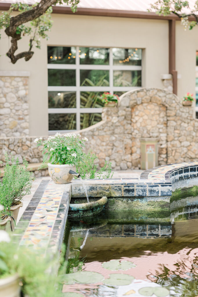 Photo of fountain outside The Veranda San Antonio Wedding venue. A flower pot with a spout flowing into a shallow pool